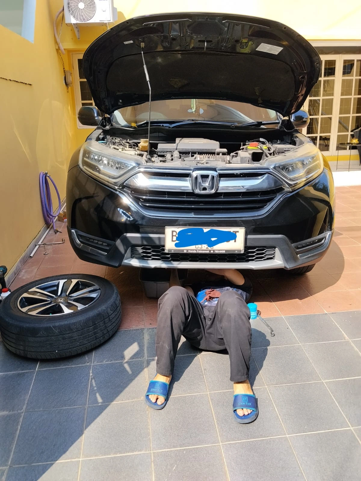 Mekanik panggilan Honda Home Service sedang merawat mobil Honda CR-V di garasi rumah pelanggan